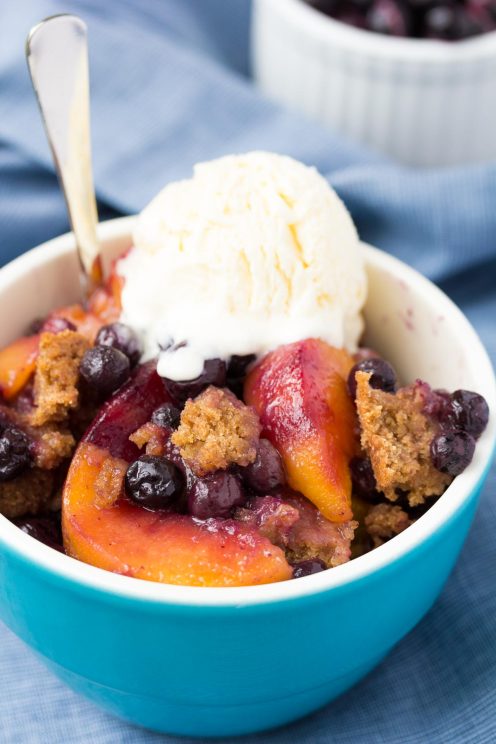 Crockpot peach cobbler with blueberries, topped with vanilla ice cream.