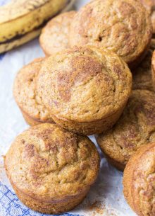 Muffins stacked together with ripe banana in the background.