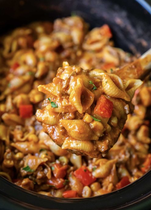 Taco pasta on a wooden spoon held above slow cooker.