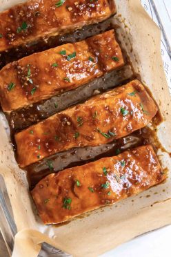 Four baked salmon fillets with glaze in a parchment paper lined baking dish.