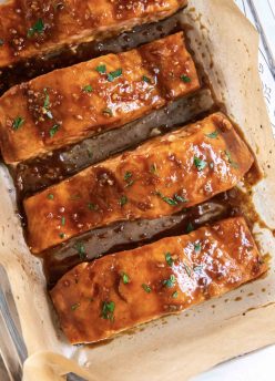 Four baked salmon fillets with glaze in a parchment paper lined baking dish.