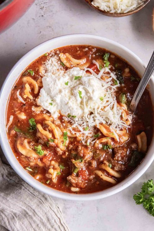 Lasagna soup in a bowl topped with ricotta, mozzarella and parmesan cheese, with a spoon.