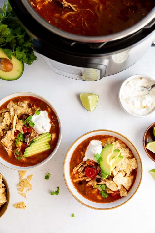 Two bowls of instant pot chicken tortilla soup with toppings with instant pot in background.