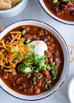 Turkey chili served in a bowl topped with sour cream, shredded cheddar, jalapenos, green onions and cilantro.