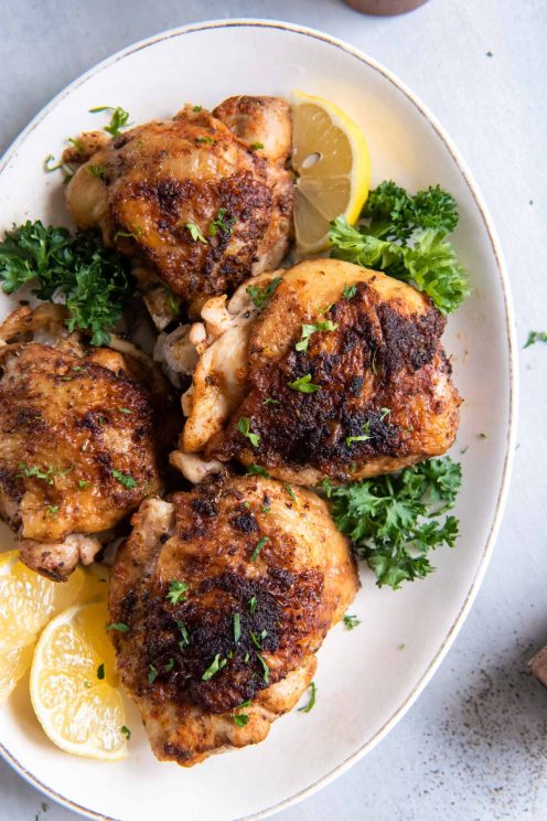Instant Pot chicken thighs on a serving plate with lemon wedges and parsley.