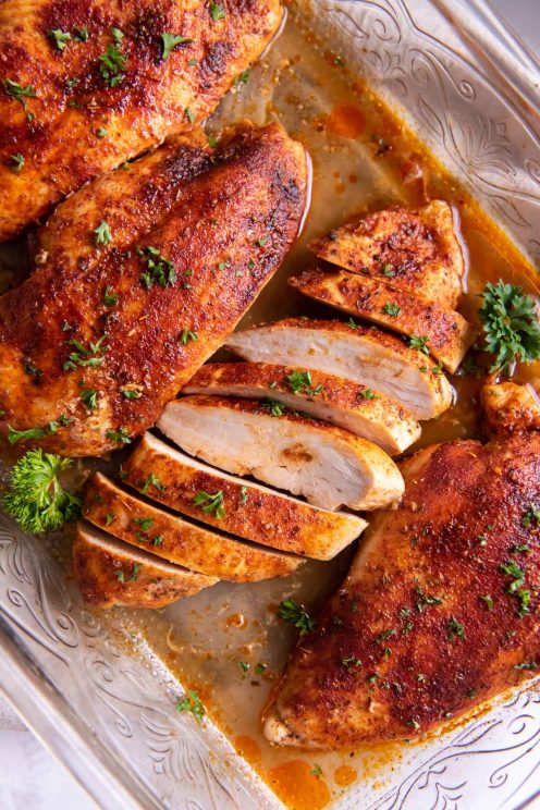 Four baked chicken breasts in baking dish with one breast sliced.