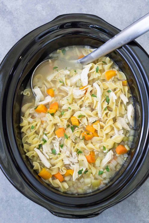 Crockpot chicken noodle soup in a slow cooker with a ladle.