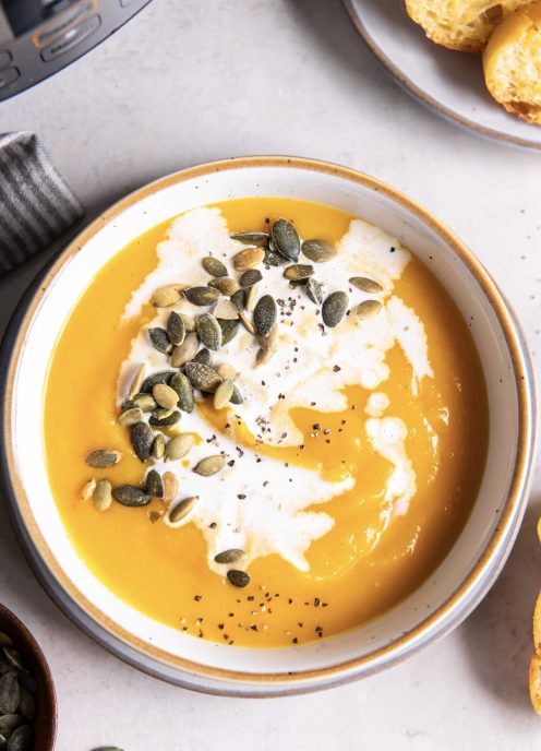 Instant pot butternut squash soup in a bowl with a drizzle of cream plus pepitas for garnish.