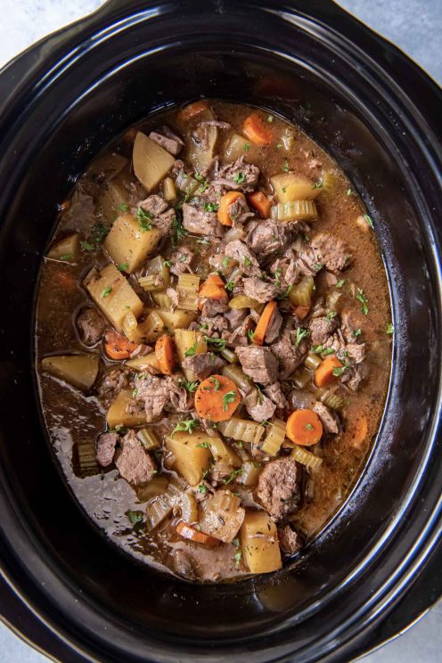 Beef stew in a slow cooker with a wooden spoon.