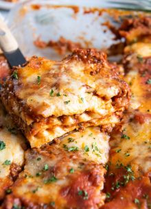 Slice of lasagna on spatula set on pan of lasagna.