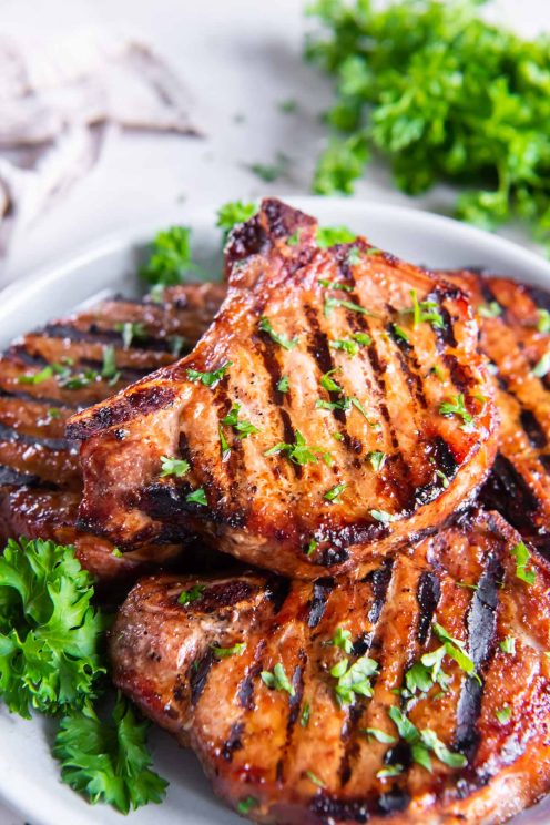 Grilled bone-in pork chops stacked on a plate.