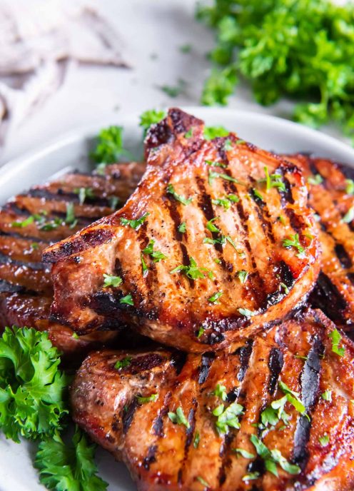 Grilled bone-in pork chops stacked on a plate.
