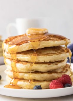 Stack of five buttermilk pancakes with maple syrup dripping down.