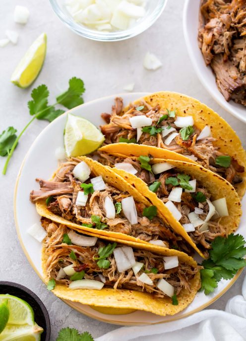 Four pork carnitas tacos on a plate.