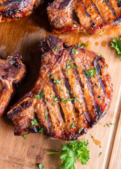 Marinated grilled pork chops on a wood cutting board.