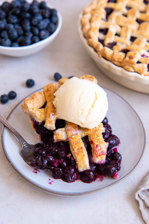 Slice of blueberry pie with scoop of vanilla ice cream on top.