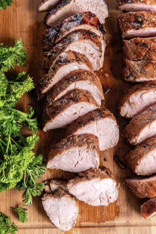 Sliced grilled pork tenderloin on a wood cutting board.
