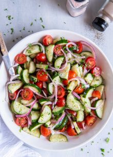 Cucumber tomato salad in a white salad bowl with serving spoon.