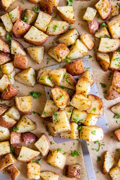 Roasted red potatoes on a sheet pan with a metal spatula.