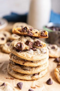 Stack of chocolate chip cookies with the top cookie broken in half to show melty chocolate chips inside.