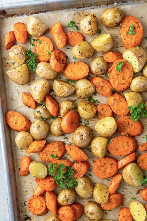 Roasted potatoes and carrots on a baking sheet with parsley garnish.