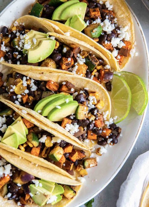 Five vegetarian tacos next to each other on an oval plate.