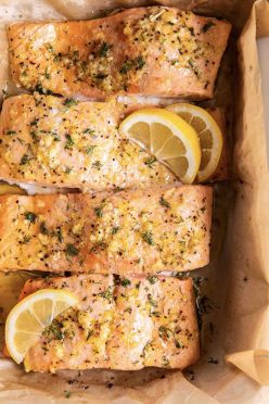 Four baked salmon fillets with lemon and garlic in baking dish.