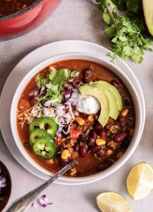 Bowl of taco soup topped with shredded cheese, sour cream, chopped red onion, sliced avocado, sliced jalapeno and fresh cilantro.