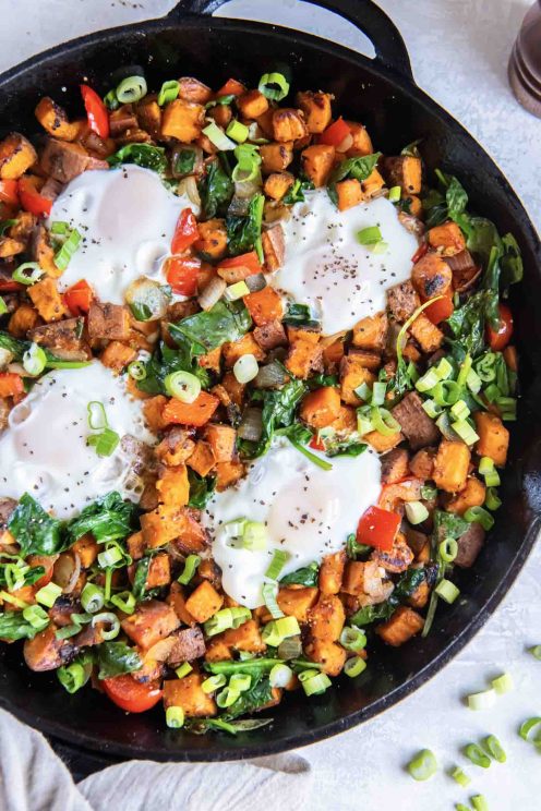 Sweet potato hash with four eggs in a cast iron skillet.