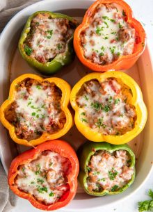 Six baked stuffed bell peppers in baking dish.