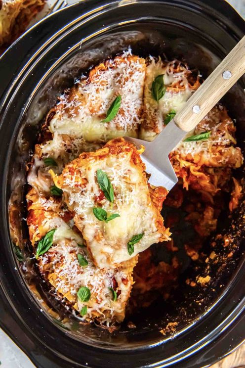 Slice of lasagna on a spatula resting on top of lasagna in slow cooker.