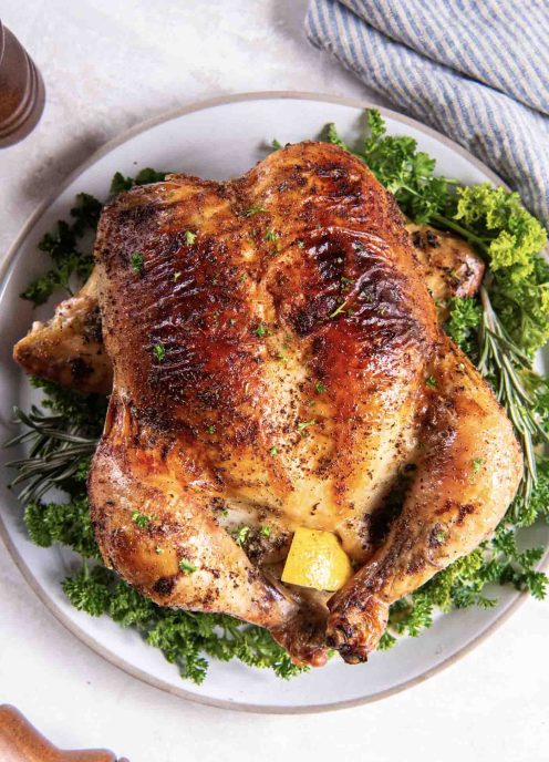 Whole roasted chicken on a plate garnished with fresh herbs.
