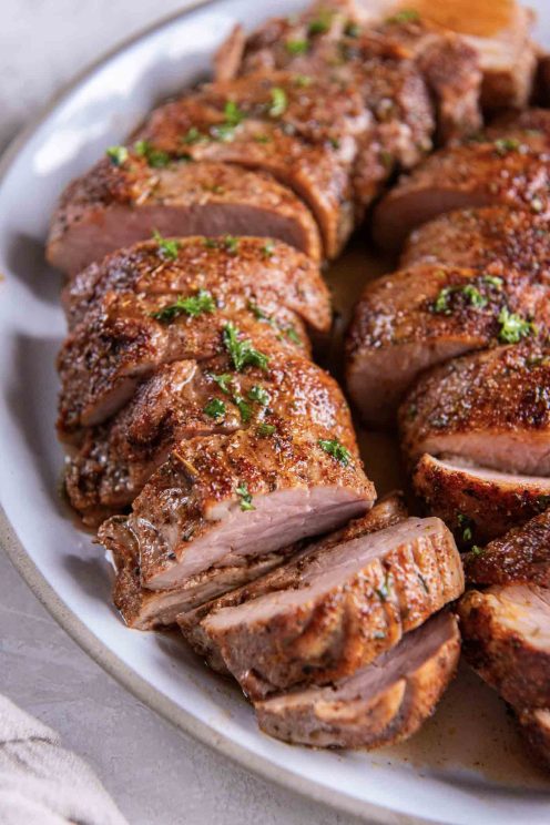 Close up of sliced pork tenderloin on a white serving plate.