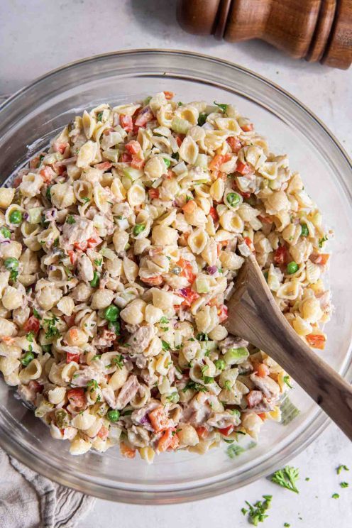 Tuna pasta salad in a glass bowl with a wooden spoon.