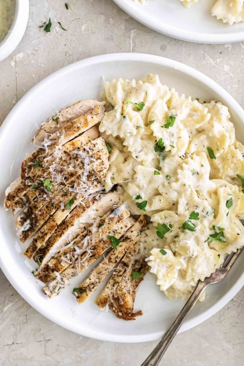 Alfredo pasta and sliced chicken breast served on a white plate with a fork.