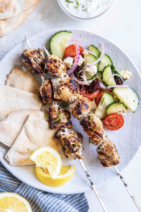 Two chicken souvlaki skewers served with Greek salad and pita bread.