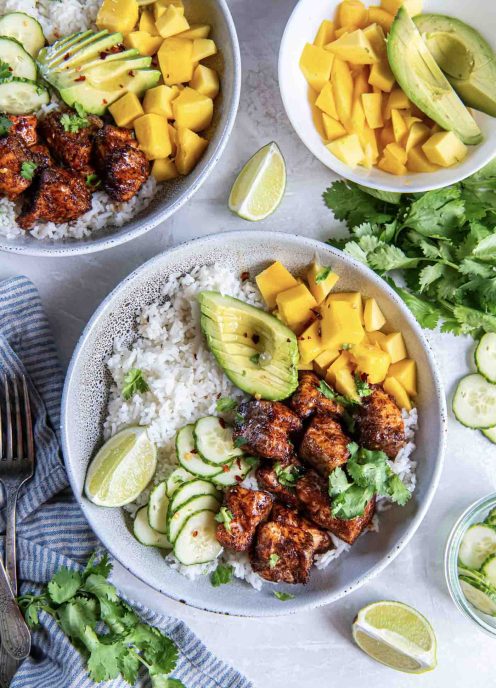 Two salmon bowls with white rice, seasoned salmon pieces, mango, avocado and cucumber.