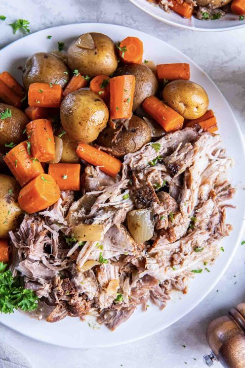 Shredded pork roast with potatoes and carrots on a serving plate.