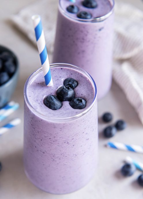 Blueberry smoothie in a glass topped with four fresh blueberries and a blue and white striped straw.