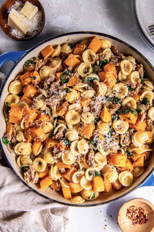 Butternut squash sausage pasta in a skillet garnished with grated Parmesan cheese and red pepper flakes.