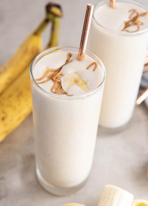 Smoothie served in two tall glasses with a drizzle of peanut butter, banana slices and a straw.