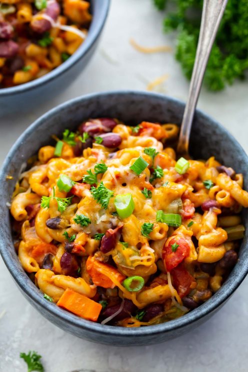 Chili mac topped with cheese and green onions in a bowl with a spoon.