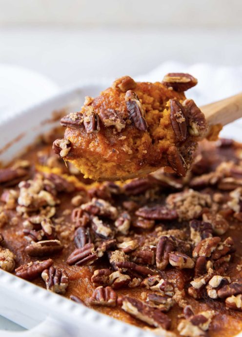 Spoonful of sweet potato casserole held over casserole in baking dish.