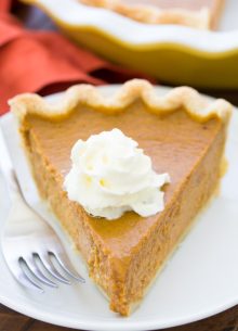 A slice of homemade pumpkin pie with whipped cream on a small plate.