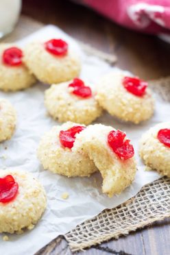 Cherry cream cheese cookies arranged on parchment paper with a bite out of one cookie.